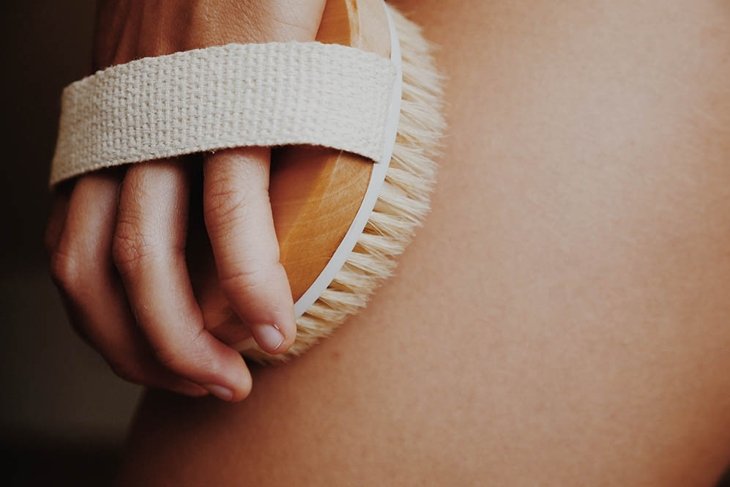 Woman's arm holding dry brush to top of her leg