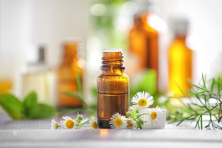 Bottle with essential oil and chamomile flowers on wooden table