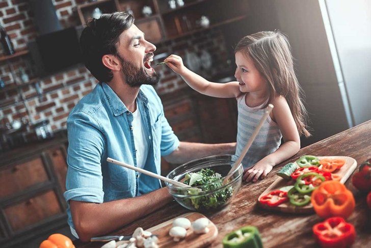 Handsome man and his little cute daughter are cooking on kitchen. Making salad. Healthy lifestyle concept.