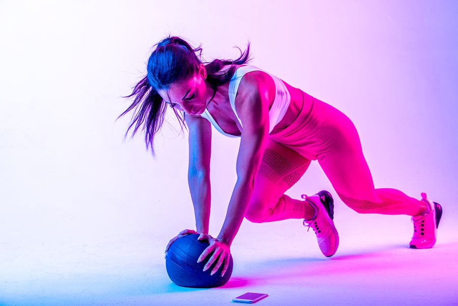 woman doing mountain climbers exercise on medicine ball with magenta and blue lights