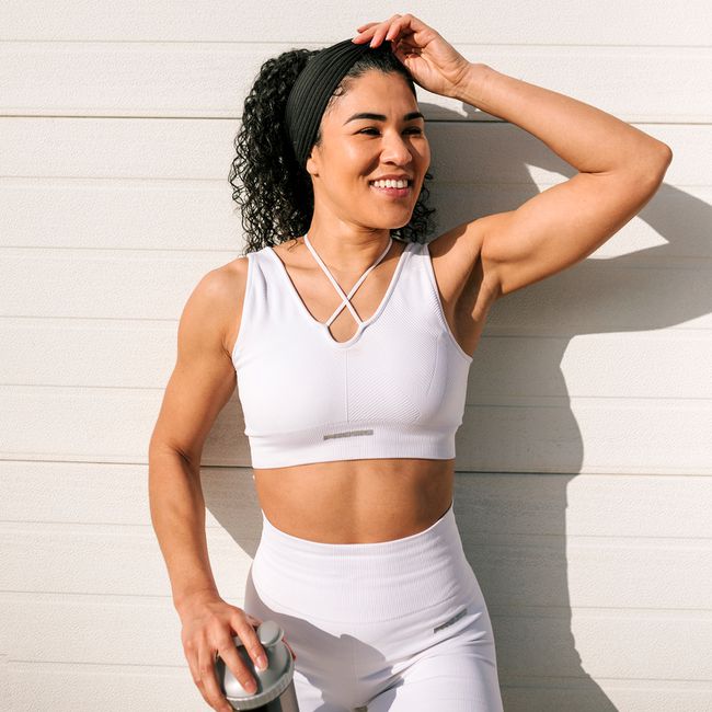 Happy sportswoman with hand in hair looking away against wall on sunny day